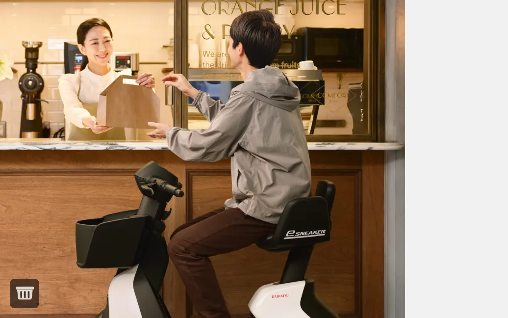 画像：コーヒースタンドでテイクアウトを受け取る、e-SNEAKERに乗った男性